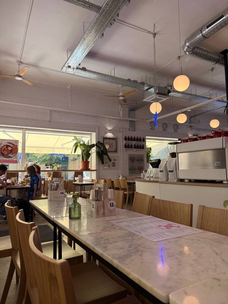 Babka Deli interior — marble tables, wooden chairs and a coffee machine by the window